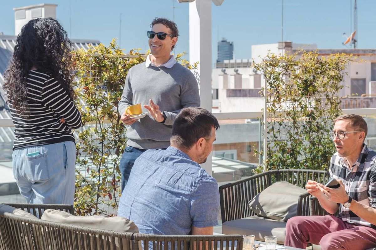 Imagen de 4 personas charlando animadamente en la terraza soleada de un edificio.